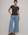Alex is 5'8" and wearing P Baby Tee in Espresso Brown paired with light wash wide leg denim trousers