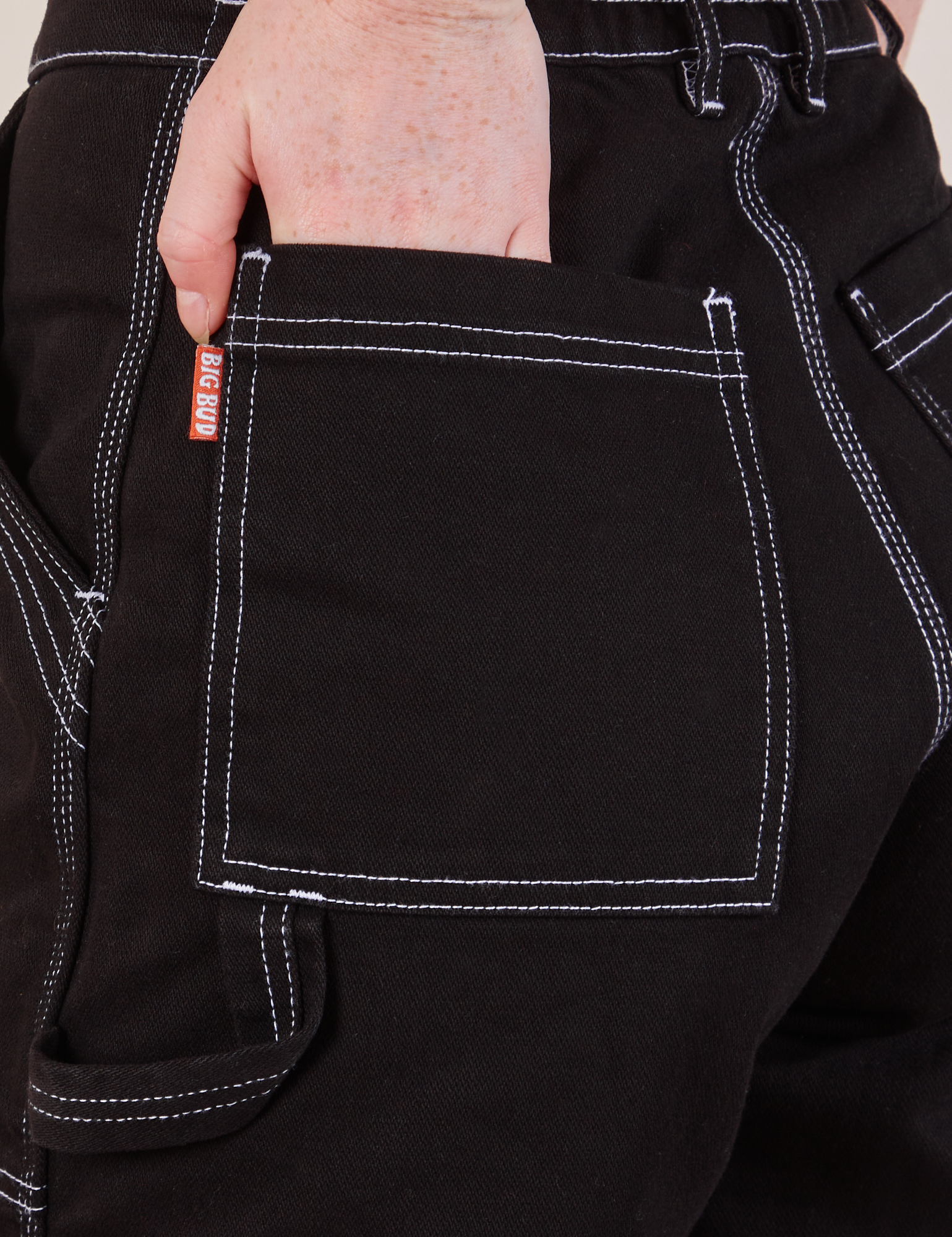 Carpenter Shorts in Basic Black back pocket close up. Margaret has her hand in the pocket.