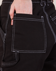 Carpenter Shorts in Basic Black back pocket close up. Margaret has her hand in the pocket.