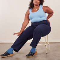 Morgan is sitting on a vintage stool wearing Work Pants in Navy Blue and a baby blue Tank Top