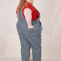 Back view of Railroad Stripe Denim Original Overalls and paprika Baby Tee worn by Catie. Catie has her hand in the back pocket.