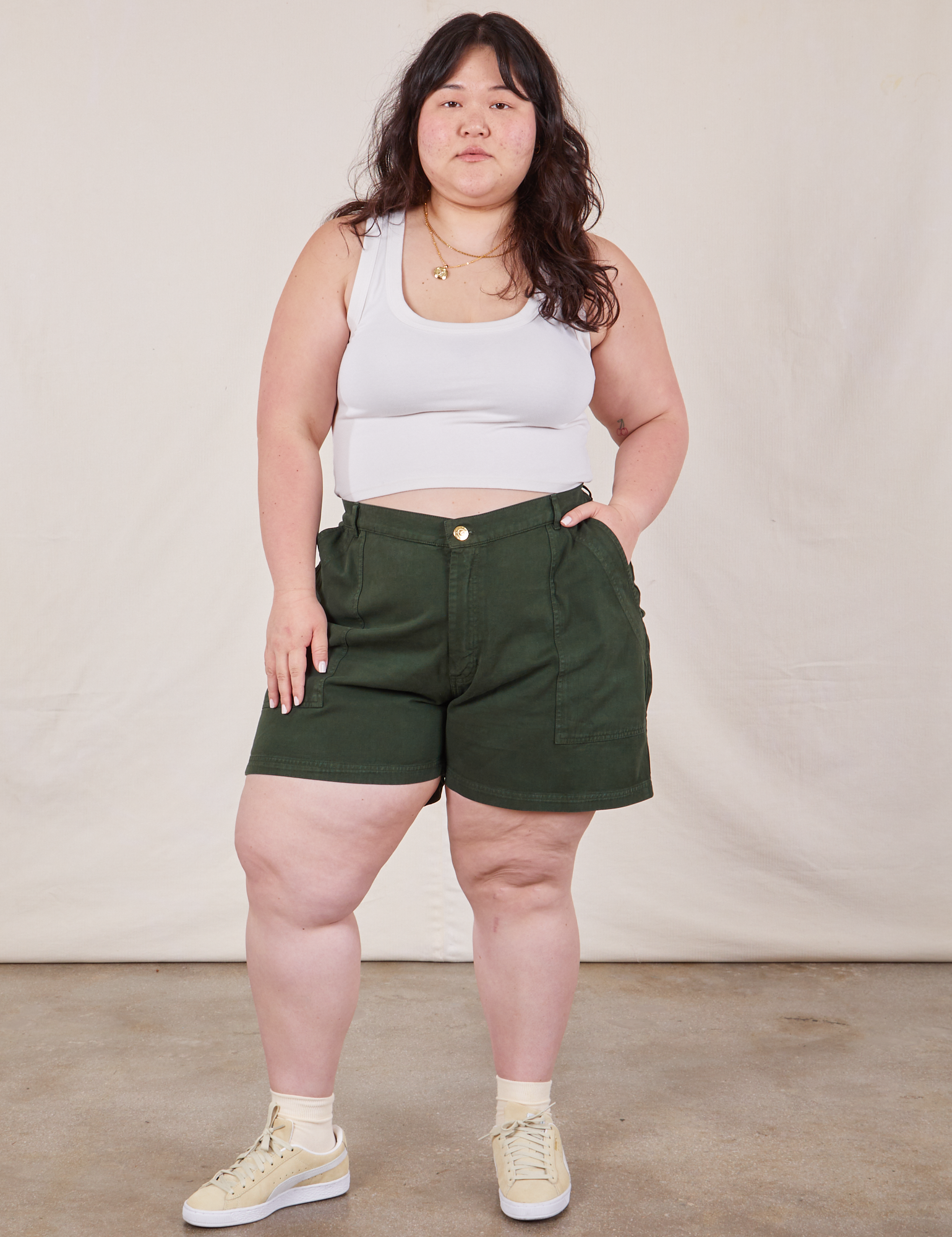 Ashley is 5’7” and wearing 1XL Classic Work Shorts in Swamp Green paired with a Cropped Tank Top in vintage tee off-white