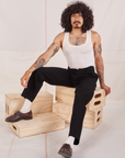 Jesse is sitting on a stack of wooden crates. They are wearing Denim Trouser Jeans in Black and a Tank Top in vintage tee off-white