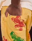 Close up of Isaac's hand in the back pocket of Gummy Bear Paintstamped Work Pants in Butter Yellow