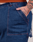 Carpenter Shorts in Dark Wash front pocket close up. Sam has their hand in the pocket.
