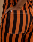 Close up of Kandia's hand in the back pocket of Black Stripe Work Pants in Construction Orange
