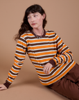 Alex is sitting on the floor and wearing Long Sleeve Striped Burly Tee in Orange