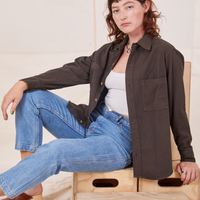 Alex is sitting on a wooden crate. She is wearing Oversize Overshirt in Espresso Brown, vintage off-white Tank Top and light wash Frontier Jeans