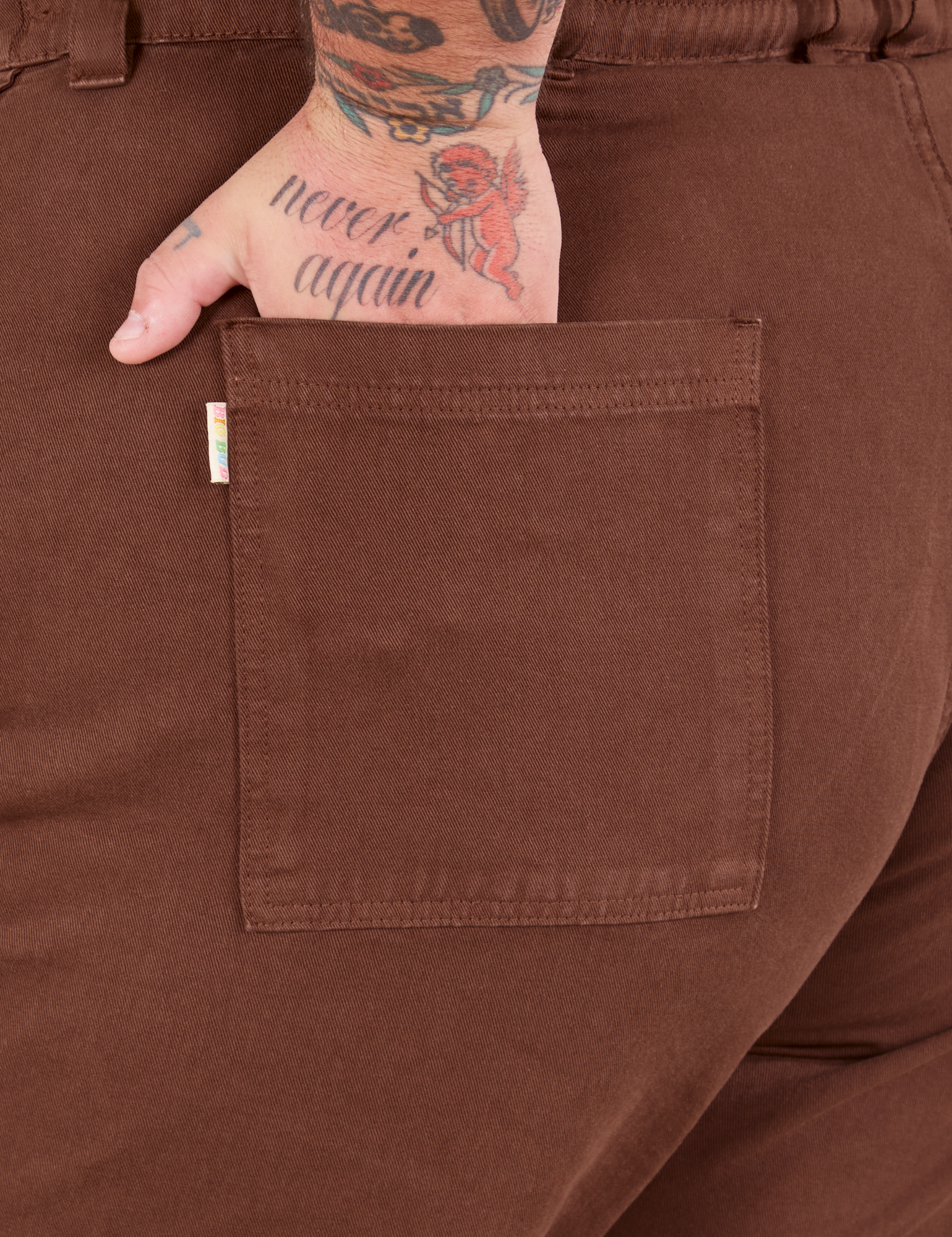 Bell Bottoms in Fudgesicle Brown back pocket close up. Sam has their hand in the pocket.
