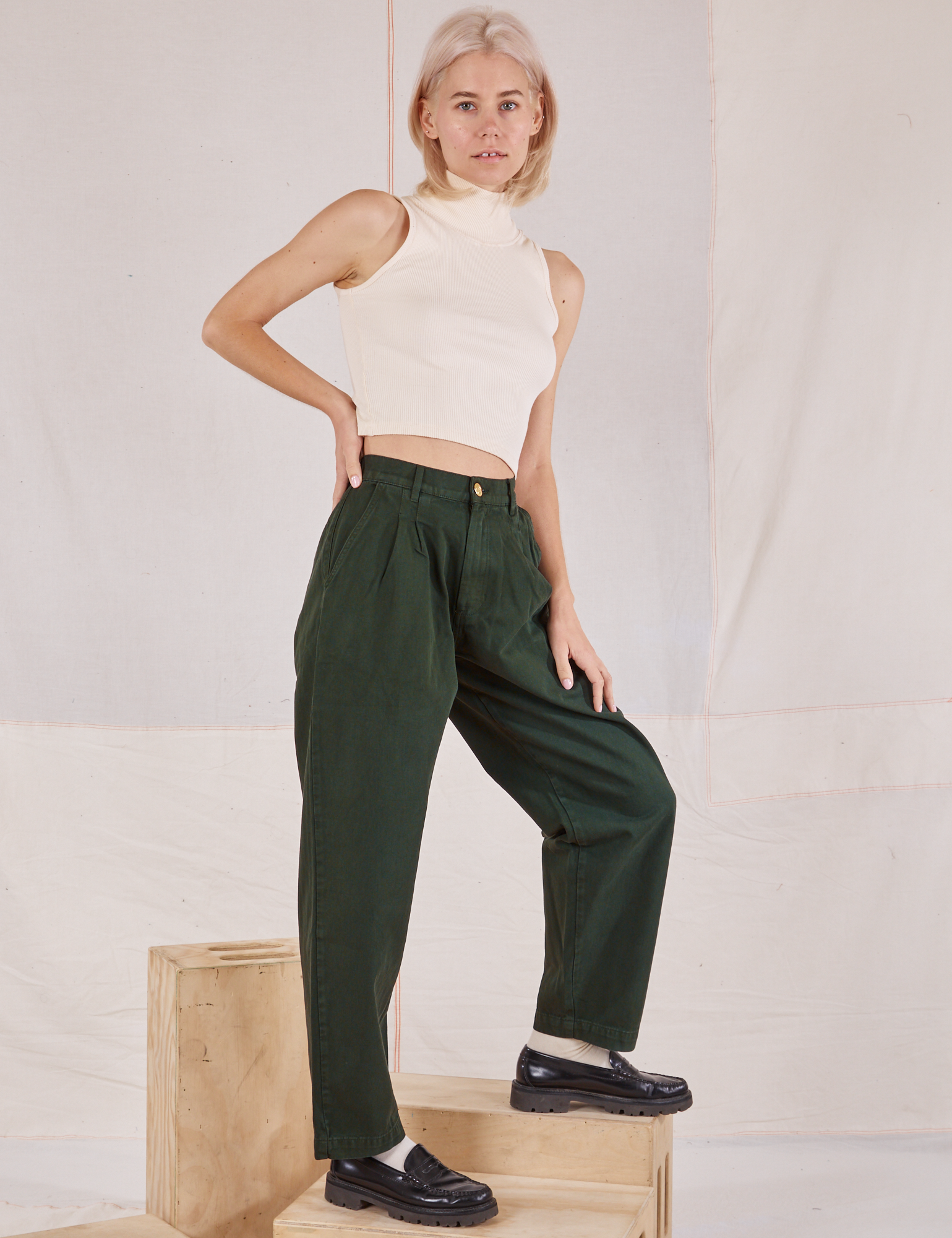 Angled front view of Heavyweight Trousers in Swamp Green and vintage tee off-white Sleeveless Turtleneck on Madeline