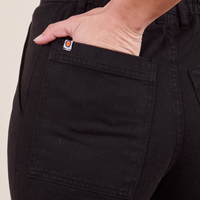 Back pocket close up of Work Pants in Basic Black. Soraya has her hand in the pocket