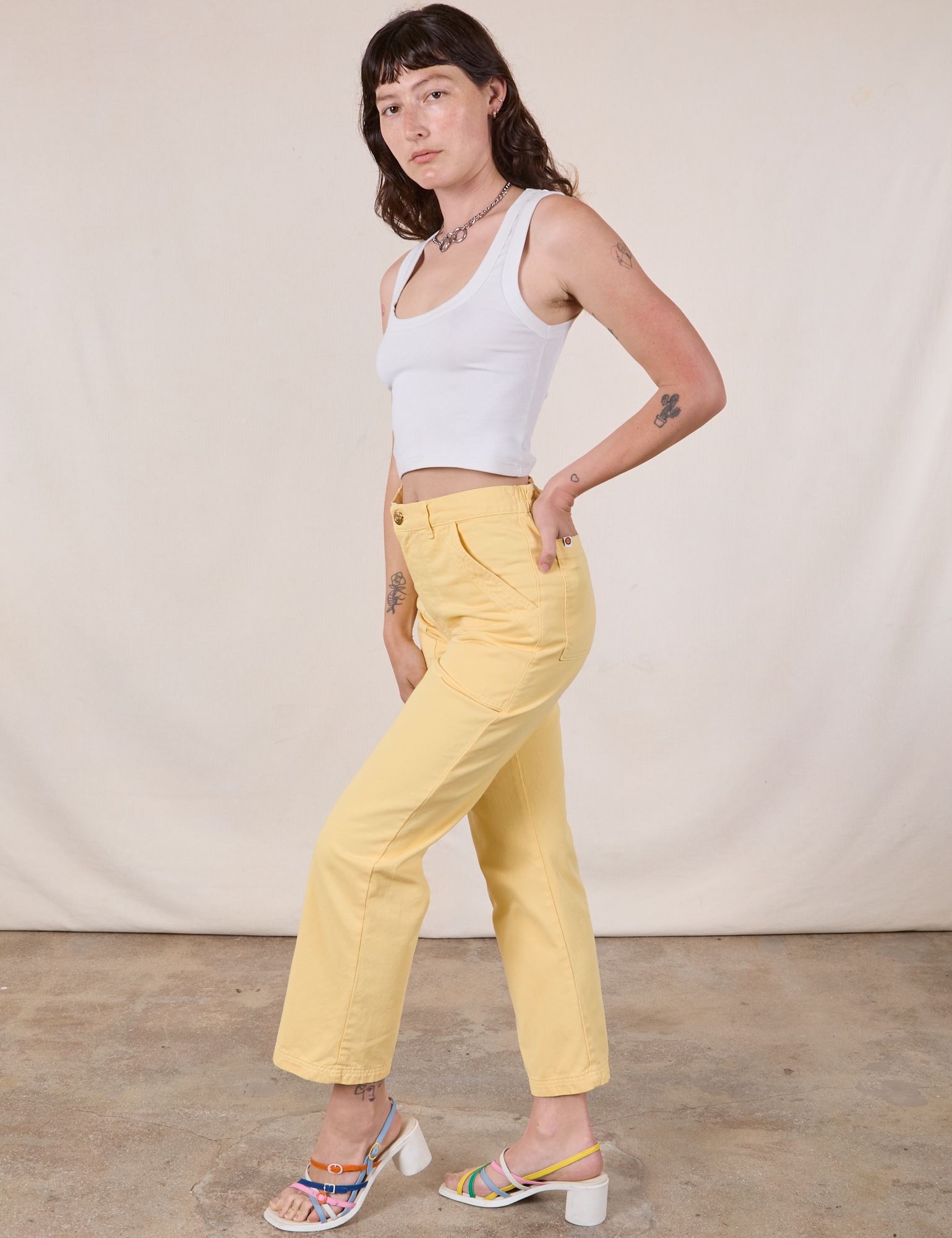 Side view of Work Pants in Butter Yellow and Cropped Tank in vintage tee off-white on Alex