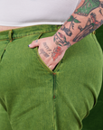 Side view close up of Overdyed Wide Leg Trousers in Gross Green. Sam has their hand in the pocket.