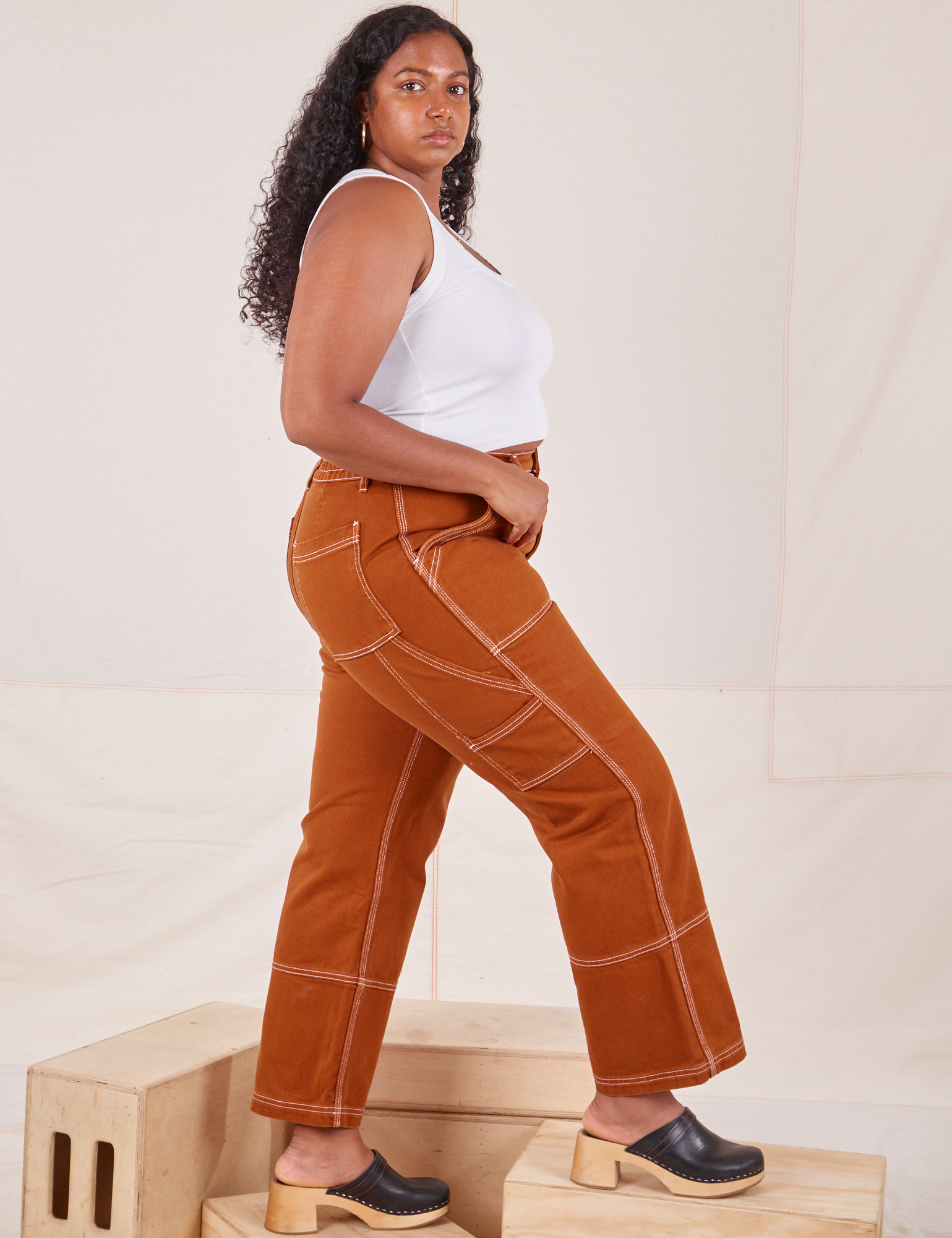 Side view of Carpenter Jeans in Burnt Terracotta and Cropped Tank Top in vintage tee off-white on Meghna