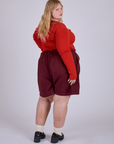Angled back view of Pleated Trouser Shorts in Red Wine and mustang red Long Sleeve Gingham Baby Tee