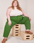 Catie is sitting on a stack of wooden crates. She is wearing Heavyweight Trousers in Lawn Green and Sleeveless Turtleneck in vintage tee off-white