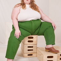 Catie is sitting on a stack of wooden crates. She is wearing Heavyweight Trousers in Lawn Green and vintage off-white Sleeveless Turtleneck.