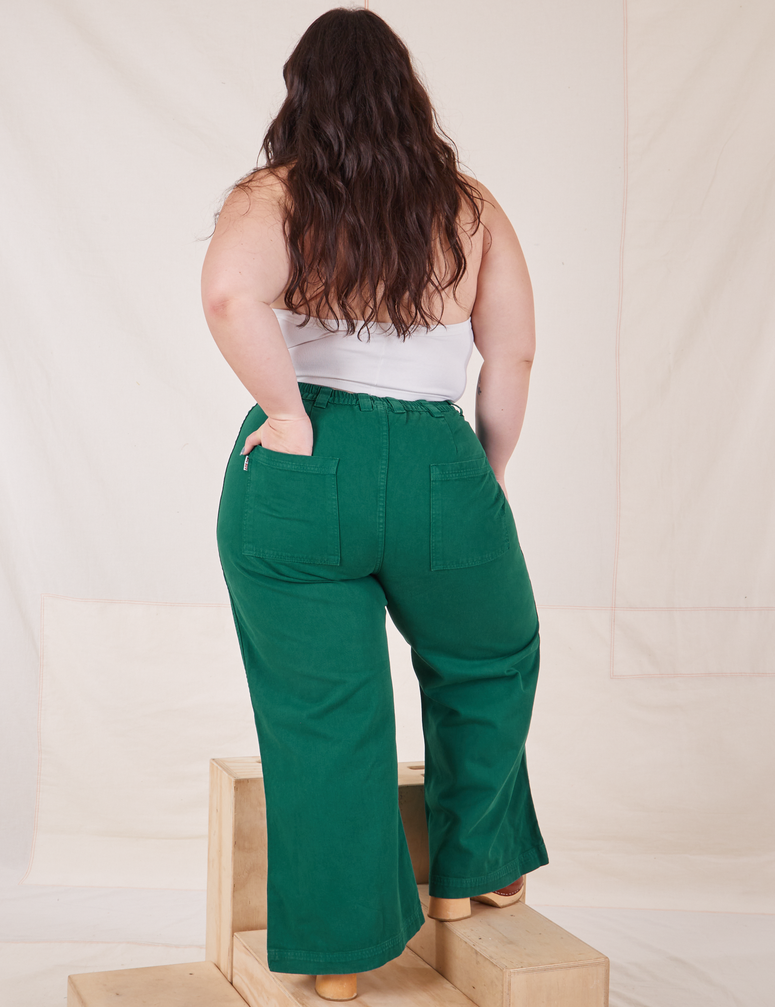 Back view of Bell Bottoms in Hunter Green worn by Ashley. She has one hand in the pocket.