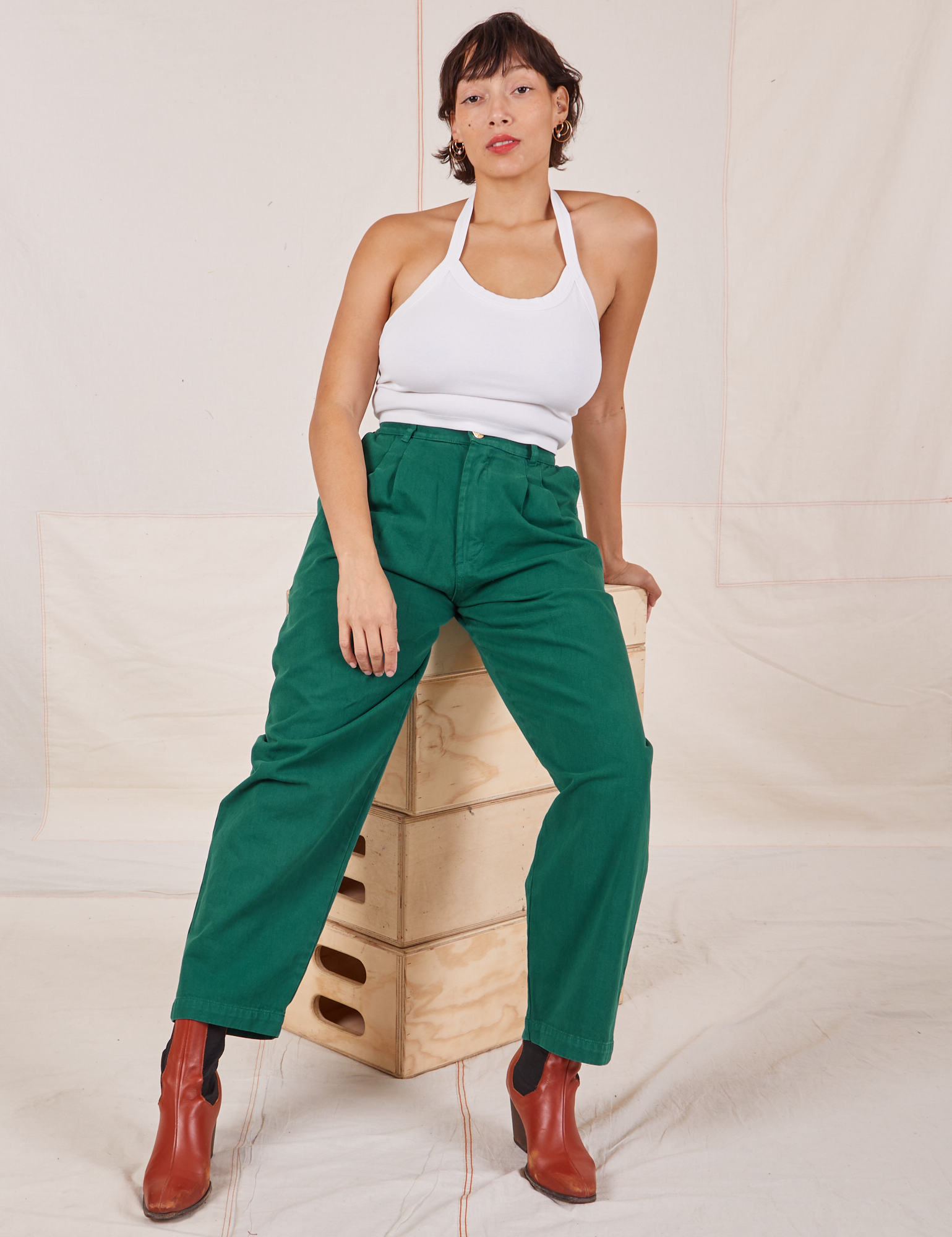 Tiara is sitting on a stack of wooden crates wearing Heavyweight Trousers in Hunter Green and Halter Top in vintage tee off-white