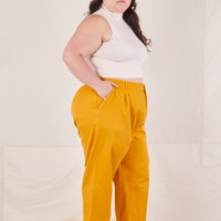 Side view of Organic Trousers in Mustard Yellow and vintage off-white Sleeveless Essential Turtleneck worn by Ashley