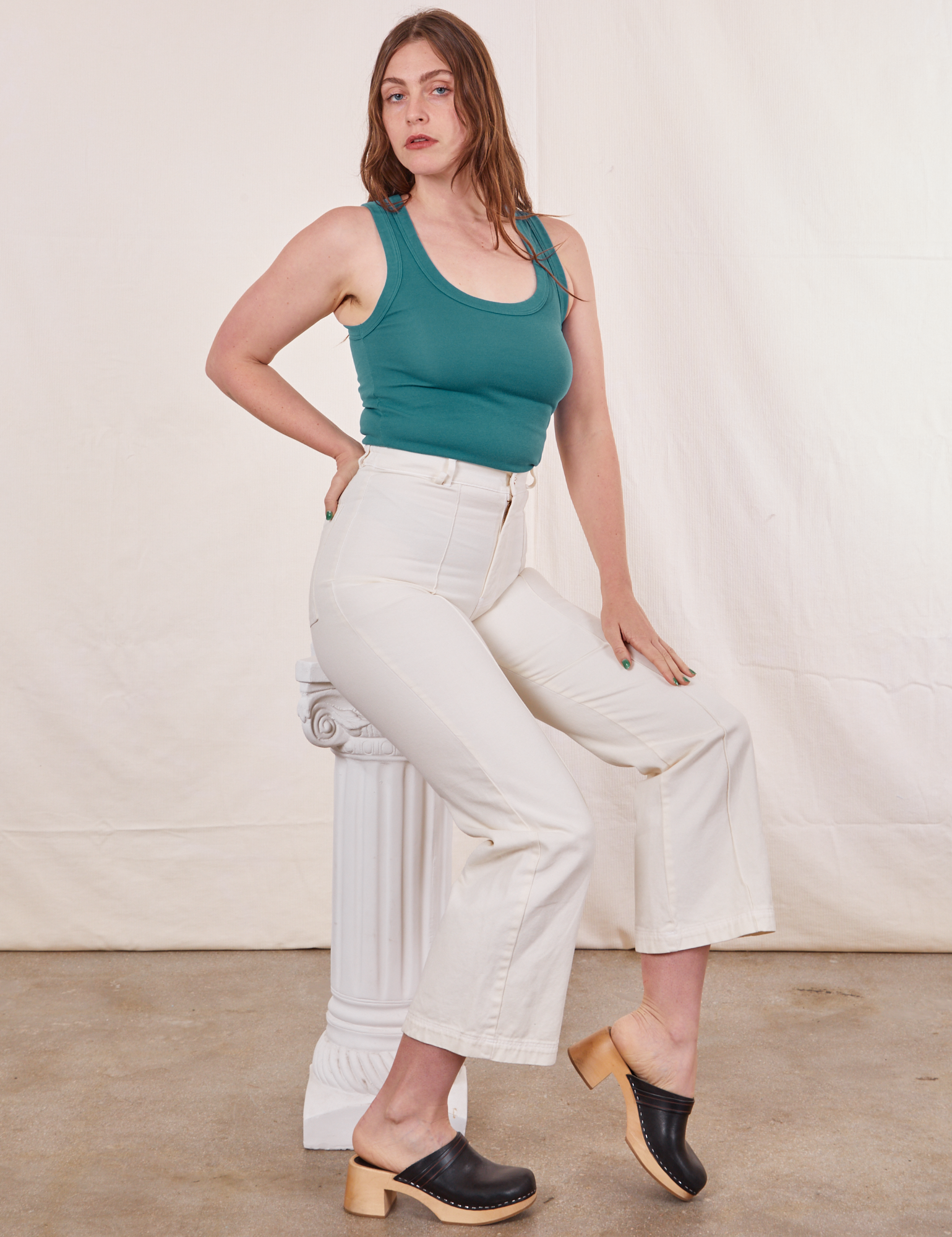 Allison is sitting on a white column wearing Tank Top in Marine Blue paired with vintage tee off-white Western Pants