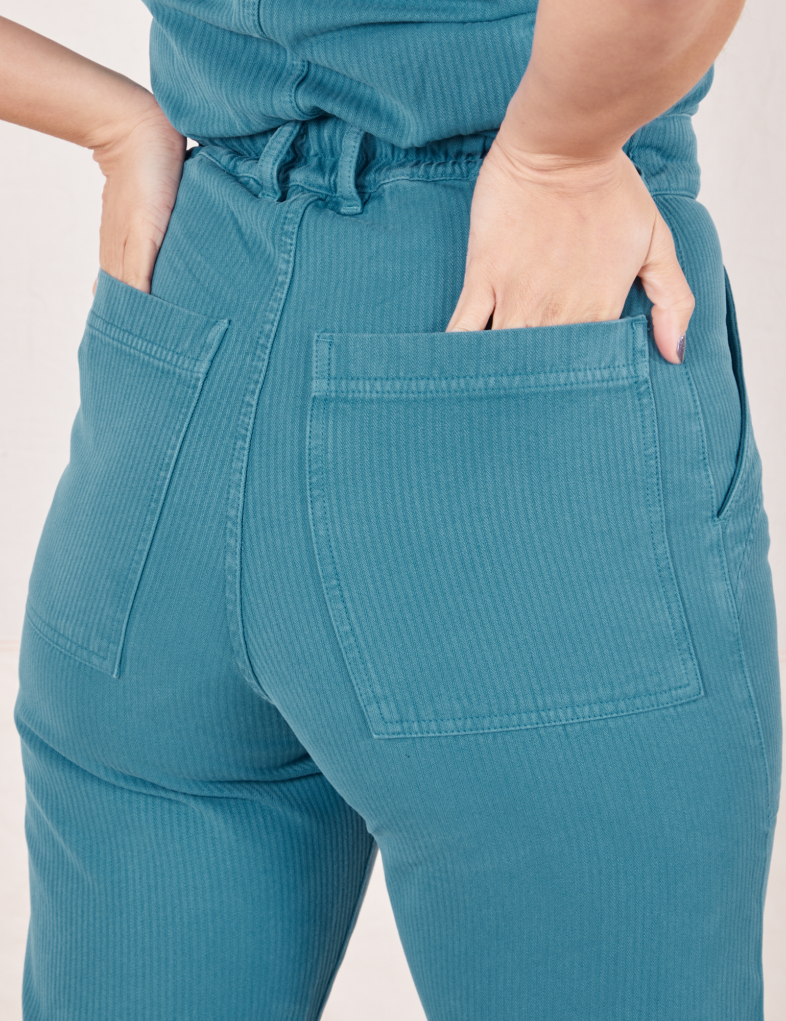 Back pocket close up of Heritage Short Sleeve Jumpsuit in Marine Blue. Tiara has both her hands in the pockets.