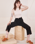 Hana is sitting on a wooden crate. She is wearing Heritage Westerns in Basic Black paired with Sleeveless Turtleneck in vintage tee off-white
