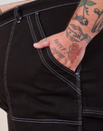 Carpenter Shorts in Basic Black front pocket close up. Sam has their hand in the pocket.