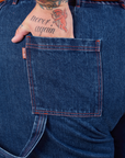 Carpenter Shorts in Dark Wash back pocket close up. Sam has their hand in the pocket.