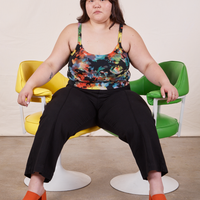 Ashley is sitting in between a yellow and green vintage chair. She is wearing Cropped Cami in Rainbow Magic Waters paired with black Petite Western Pants