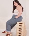 Ashley is sitting sideways on a stack of wooden crates. She is wearing Denim Trouser Jeans in Railroad Stripe and Tank Top in vintage tee off-white