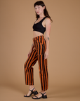 Side view of Black Stripe Work Pants in Construction Orange and black mini crop tank on Alex