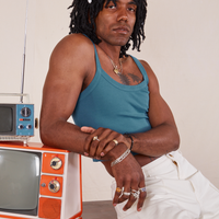 Jerrod is sitting on a vintage tv and has his elbow on a smaller vintage tv. They are wearing Cropped Cami in Marine Blue and vintage off-white Western Pants