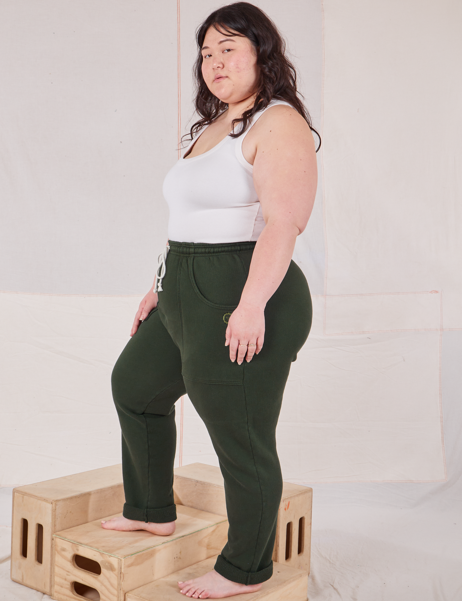 Side view of Rolled Cuff Sweat Pants in Swamp Green and vintage off-white Cropped Tank Top on Ashley