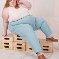 Catie is sitting on a stack of wooden crates. She is wearing Heavyweight Trousers in Baby Blue and vintage off-white Sleeveless Turtleneck