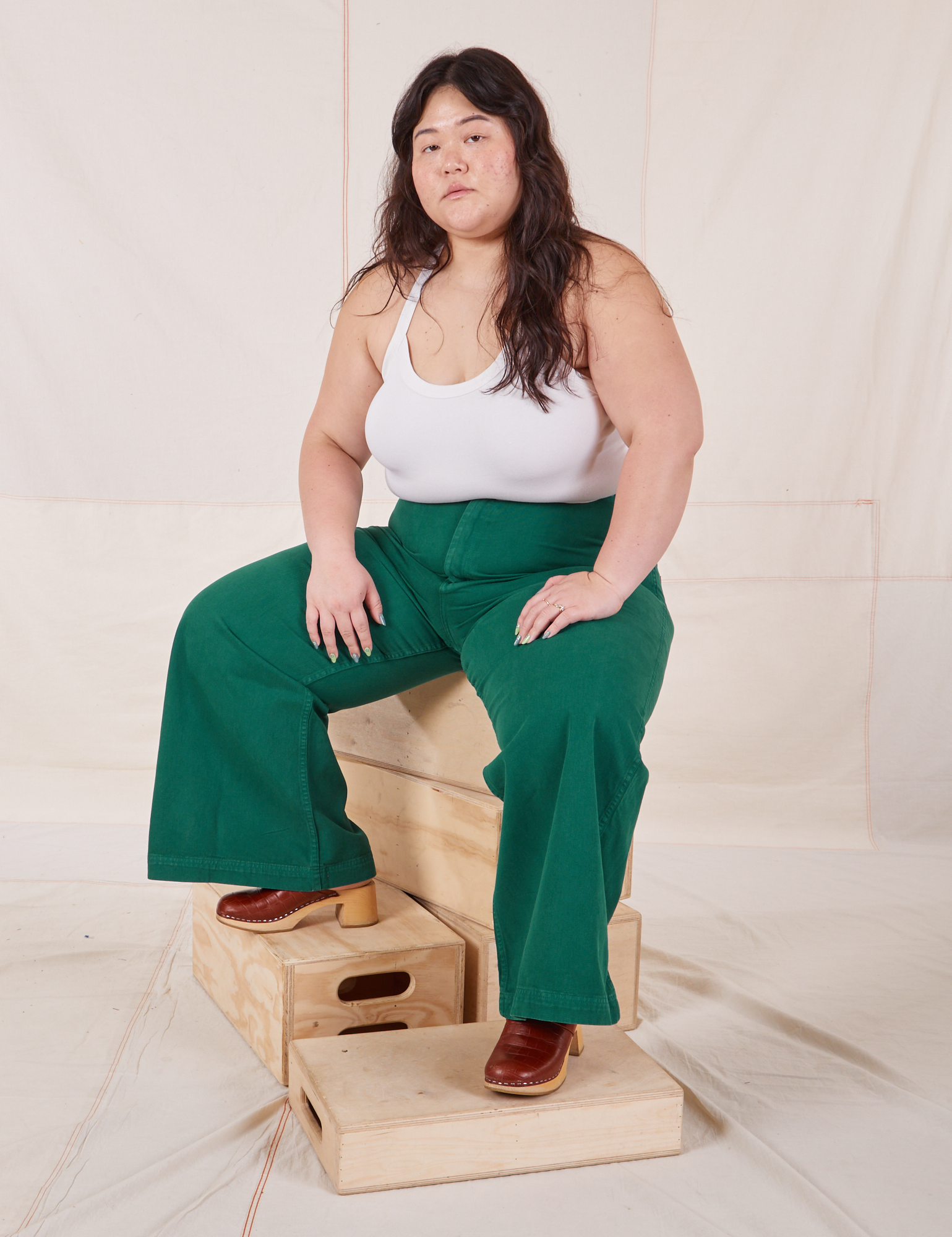 Ashley is wearing Bell Bottoms in Hunter Green and Halter Top in vintage tee off-white sitting on a wooden crate.