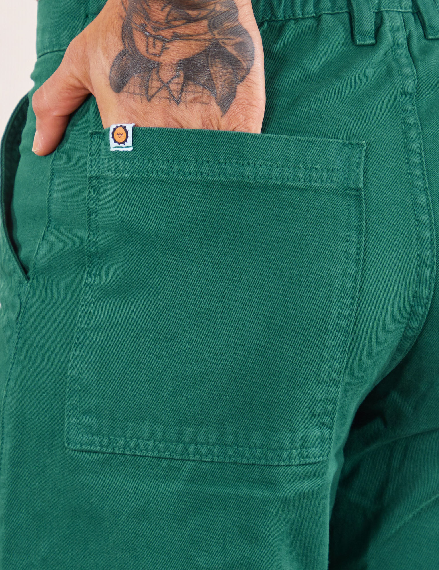 Back pocket close up of Work Pants in Hunter Green. Jesse has their hand in the pocket.