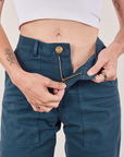 Work Pants in Lagoon front close up. Alex is pulling down the zipper tab.