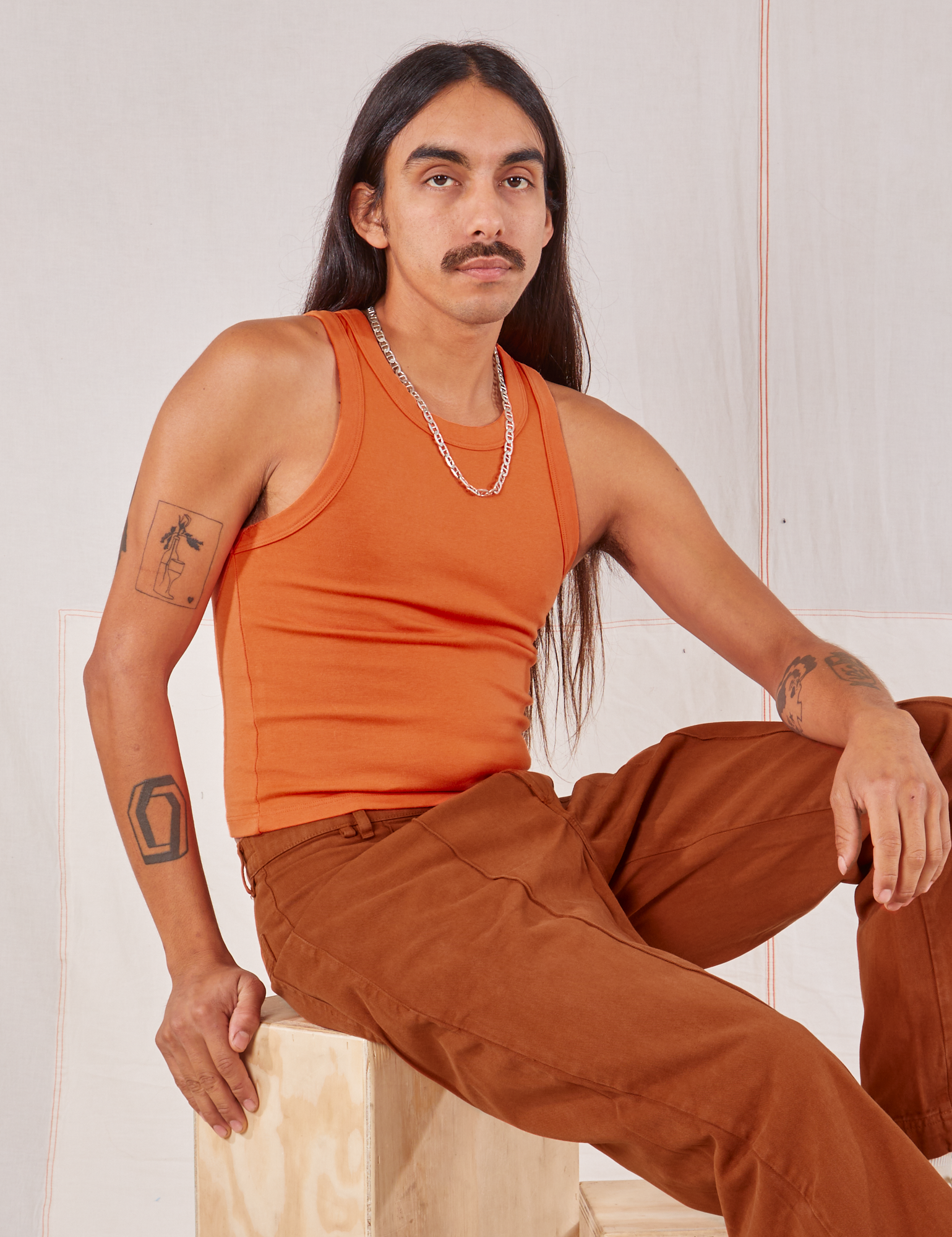 Anthony is wearing Racerback Tank in Sunset Orange and burnt terracotta Western Pants