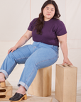 Ashley is wearing The Organic Vintage Tee in Nebula Purple and light wash Frontier Jeans. She is sitting on a wooden crate