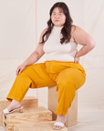 Ashley is sitting on a wooden crate wearing Organic Trousers in Mustard Yellow and Sleeveless Turtleneck in vintage tee off-white