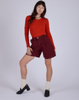 Alex is 5’8” and wearing XXS Pleated Trouser Shorts in Red Wine paired with mustang red Long Sleeve Gingham Baby Tee