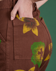 Close up of Madeline's hand in the back pocket of Floral Painted Work Pants in Brown
