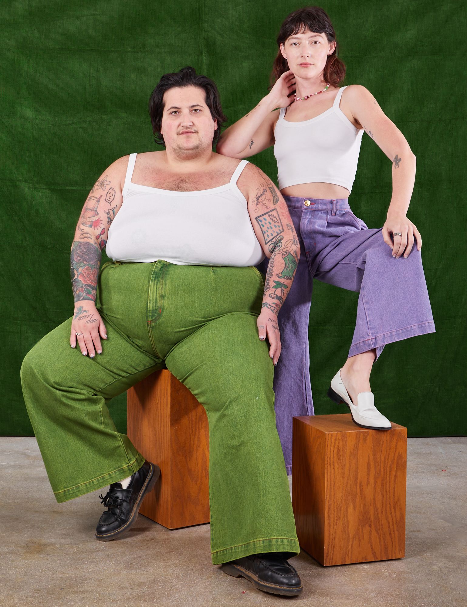 Sam is wearing Overdyed Wide Leg Trousers in Gross Green and Cropped Cami in vintage tee off-white. Alex is standing behind them wearing Overdyed Wide Leg Trousers in Faded Grape