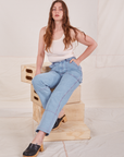 Allison is sitting on a stack of wooden crates. She is wearing Carpenter Jeans in Light Wash paired with a vintage off-white Tank Top.