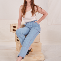 Allison is sitting on a stack of wooden crates. She is wearing Carpenter Jeans in Light Wash paired with a vintage off-white Tank Top.