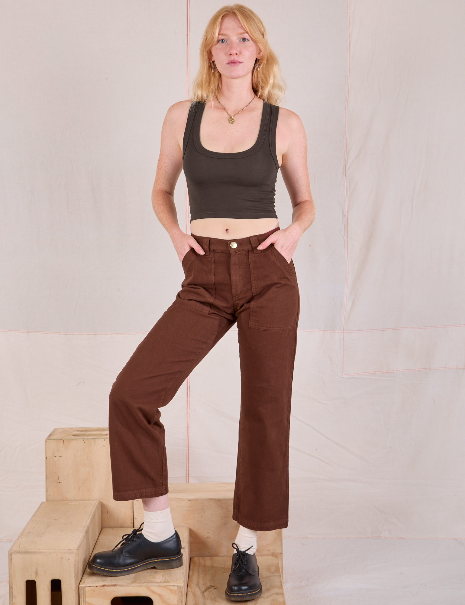 Margaret is 5'11" and wearing XS Mid-Rise Work Pants in Fudgesicle Brown paired with espresso brown Cropped Tank