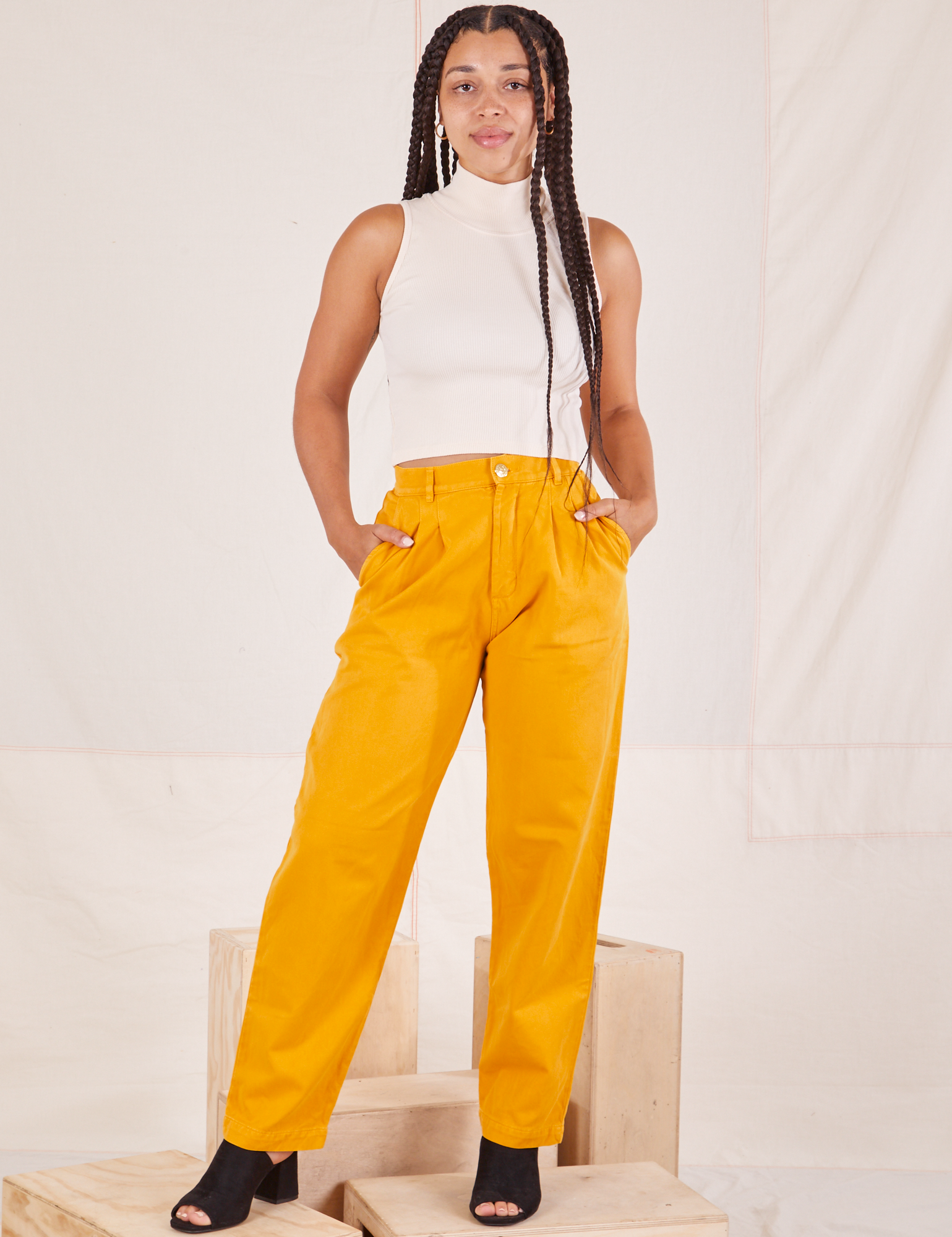 Gabi is 5&#39;7&quot; and wearing XXS Organic Trousers in Mustard Yellow paired with Sleeveless Turtleneck in vintage tee off-white