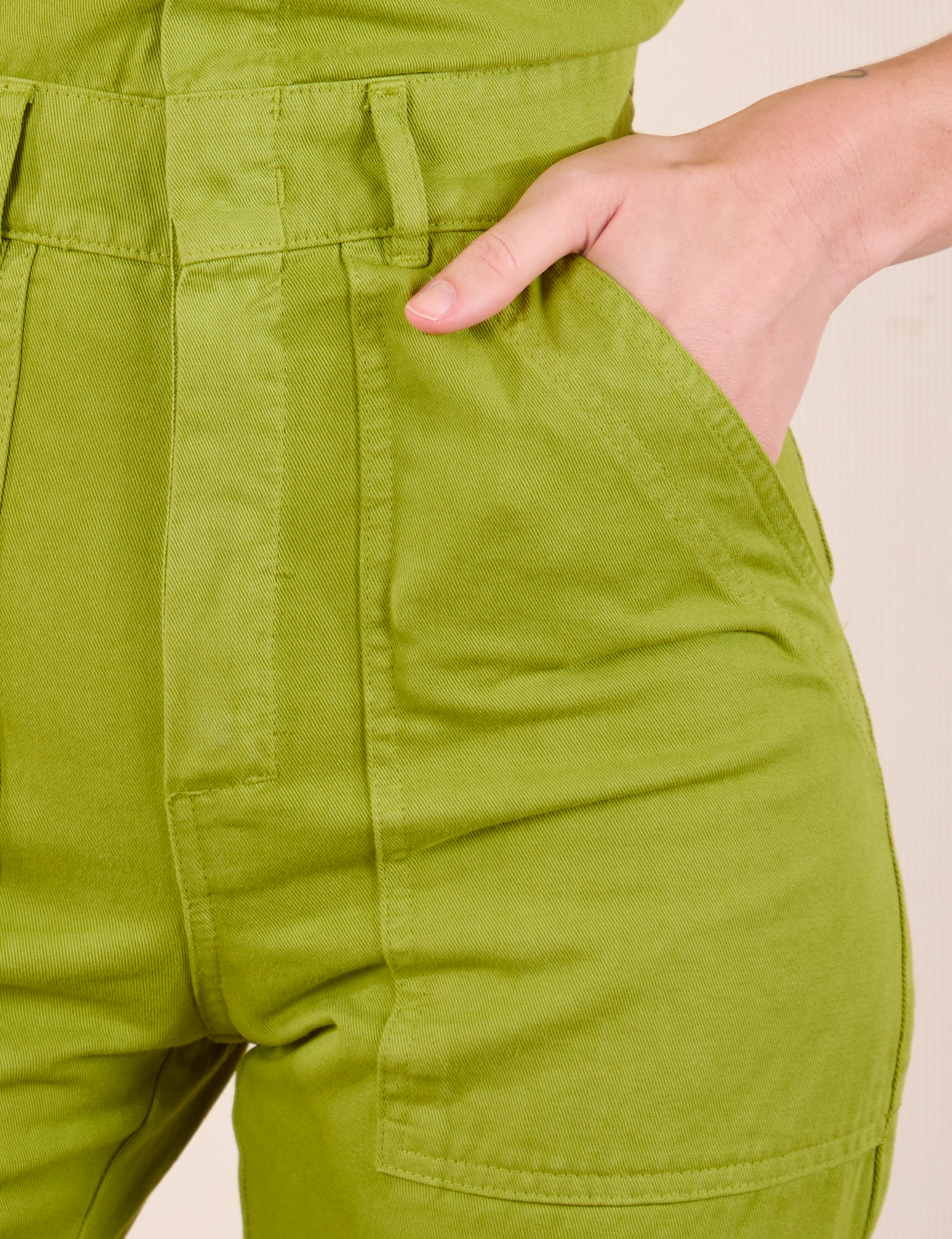 Short Sleeve Jumpsuit in Gross Green front pocket close up. Alex has her hand in the pocket.