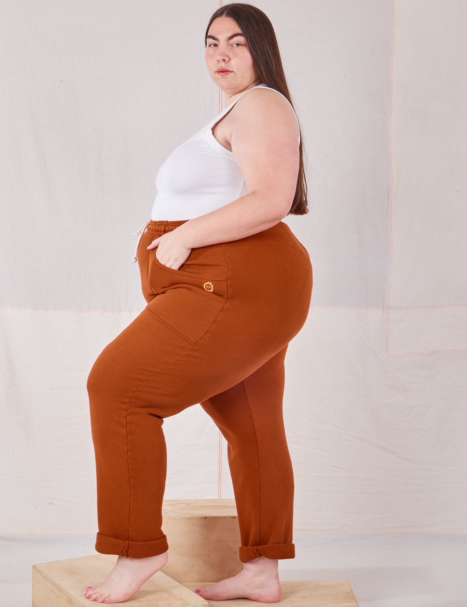 Side view of Rolled Cuff Sweat Pants in Burnt Terracotta and vintage off-white Cropped Tank on Marielena